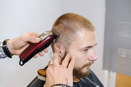 理发师用红色电动修剪器给客户剃光头图片