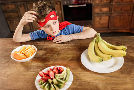 穿着红色超级英雄服装的男孩坐在厨房里图片