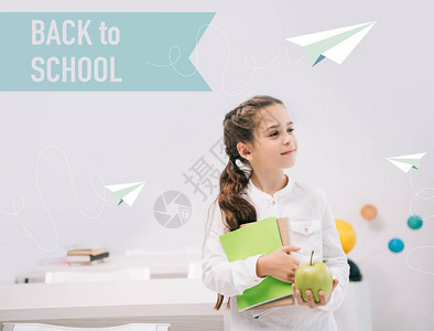 可爱的小女学生拿着青苹果和课本站在教室里图片