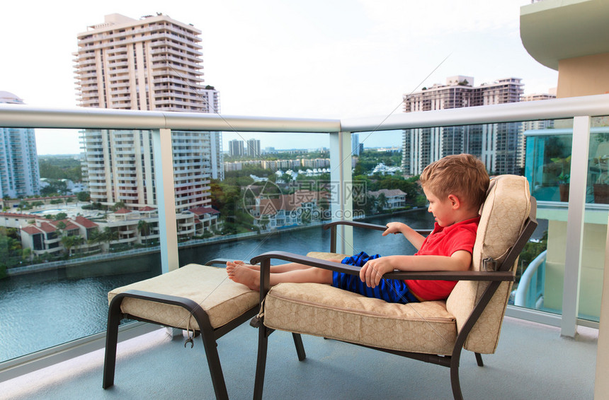 小男孩在酒店的阳台上放松看着城市景图片