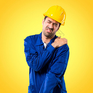 戴头盔的青年工人因在黄色背景上做努力而肩部疼痛图片