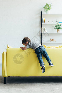 小男孩在家里的黄色沙发上爬起来图片