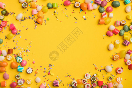 黄色背景上散落的彩色糖果和洒水的框架图片