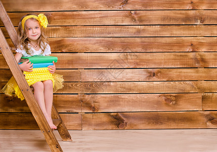 卷发小女孩形象坐在棕色木墙背景的梯子上背景