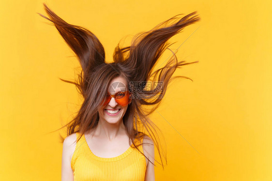 戴着橙色眼镜在黄色背景上隔离的飘扬的头发复制空间的兴奋欢快的笑声滑稽漫画女人的画像图片