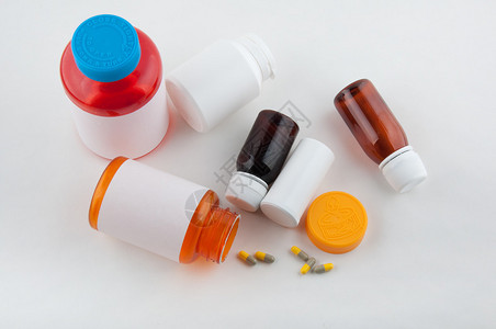 不同大小的彩色药瓶和灰黄色药丸放在白桌上图片