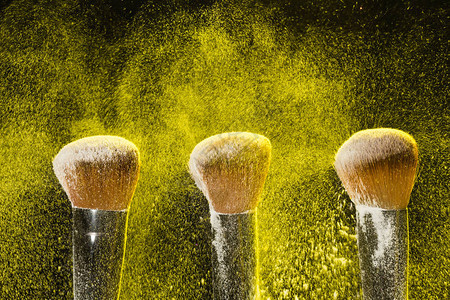 三个刷子用来化妆用黄色化妆粉在黑色背景图片