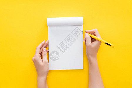 在黄色背景的空白笔记本上持有笔图片
