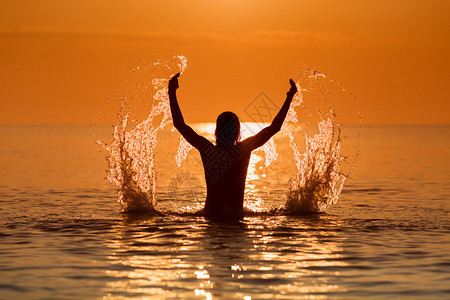 日出时男子双手在海面上泼水图片