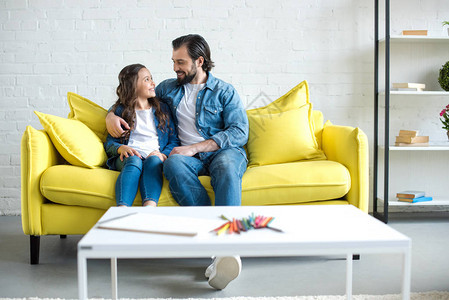 快乐的父亲和女儿坐在一起坐在黄色沙发上图片