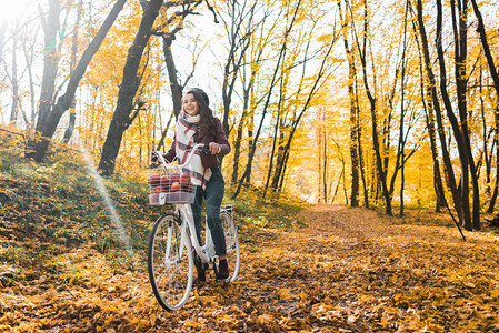 穿着皮夹克的快乐女孩和在黄色秋季森林骑自行车的贝雷特人被选择图片