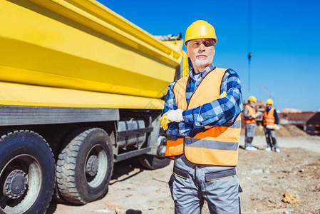 硬帽和反射背心的建筑工人在黄色卡车前用图片