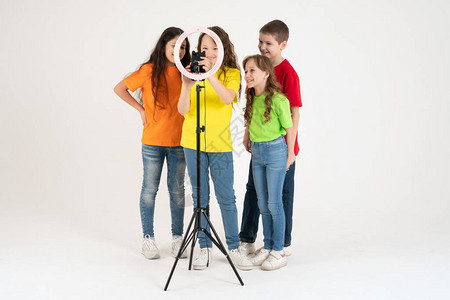 3名十几岁的女孩和一个男孩微笑并拍摄了一段视频自拍手机安装在三脚架图片