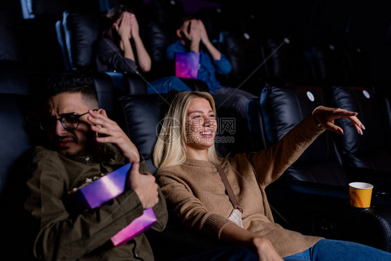 年轻微笑的女人指着大屏幕看动作片男友拿图片
