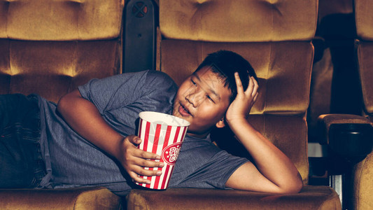 男孩正在躺下看电影快乐地吃爆米花享图片