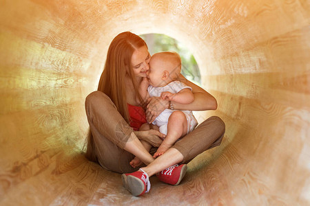 年轻的母亲和快乐的婴儿在木质隧道玩耍图片