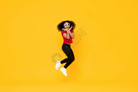 快乐的时尚非裔美国女孩在空中跳跃用手抓着黄背景图片