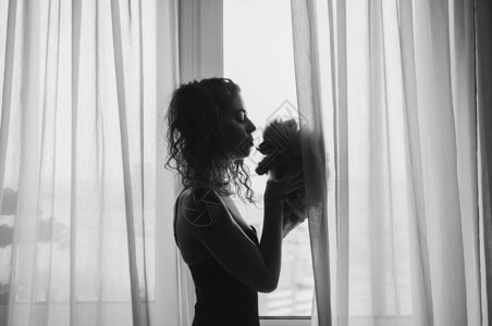 一个女孩和一只毛茸的小狗在窗户的背景上的剪影爱图片
