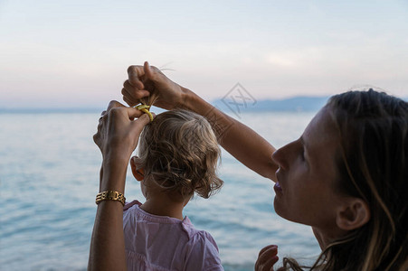 年轻母亲晚上在海边做小马尾巴和她的小孩女儿毛背景图片