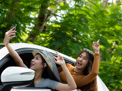 快乐的两个亚洲女人在路上的车里用智能手机给自己拍照自然背景阳光日光和树木暑假图片