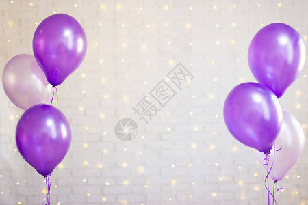 白色砖墙背景上的紫色气球与灯光图片