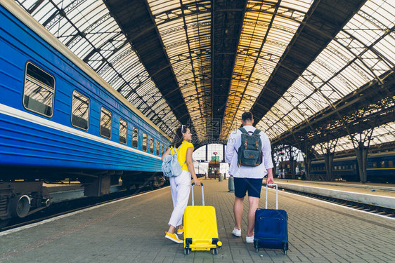 年轻夫妇在火车站步行时携带车轮旅行李箱的图片