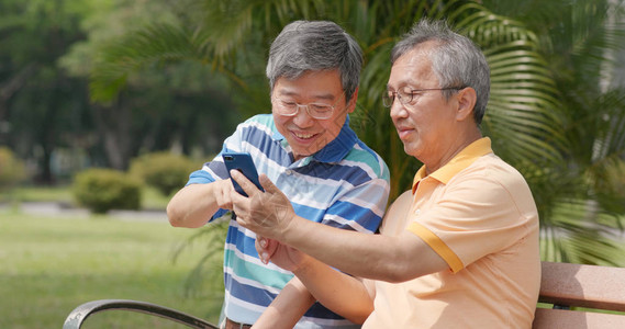 老年男朋友在户外公园聊天在手机上向其背景图片