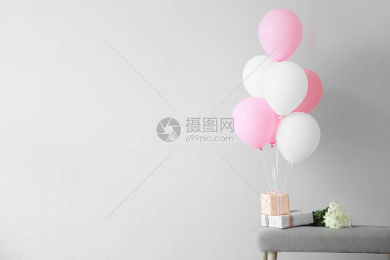 浅色背景下长凳上带礼品盒和鲜花的气球图片