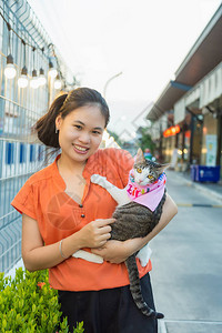 一位身着橙色衬衫的长发亚洲年轻女子在金属栅栏旁抱着一只可爱的图片