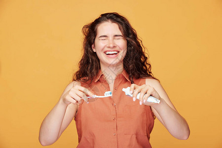 橙色背景前使用牙膏的开心女生图片