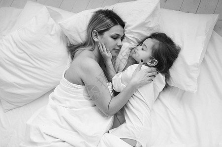 一个美丽的怀孕母亲和女儿早上在白床上玩耍图片