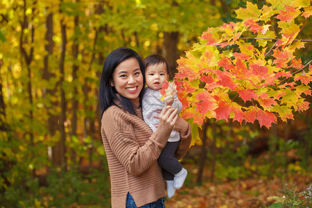 亚裔母亲在秋天公园手握着可爱的女婴外门季节与黄红叶树万圣节或感图片