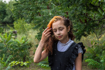 站在雨中的湿女学生女孩湿了在春天或温暖的秋天穿着校服的少年五年级的女孩染发一名女学生溅起水花的肖图片