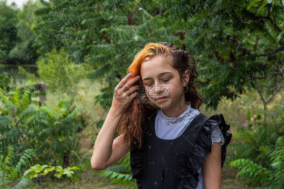 站在雨中的湿女学生女孩湿了在春天或温暖的秋天穿着校服的少年五年级的女孩染发一名女学生溅起水花的肖图片