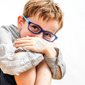 一个带着雀斑和眼镜的可爱害羞男孩的肖像图片