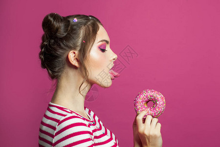 美丽的年轻女子在鲜艳的粉红色背景中舔甜圈漂亮的女图片