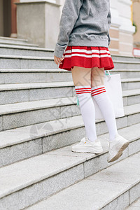 穿着高筒袜短衬衫和连帽衫的少女站在台阶上提着购物袋图片