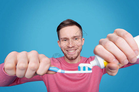 长着胡子微笑的年轻男子留着牙刷和在蓝色图片