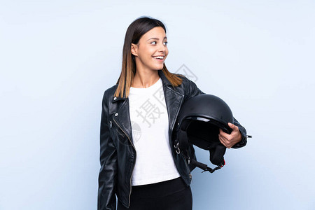 年轻的黑发年轻女人戴着摩托头盔在孤立的蓝色背景和图片