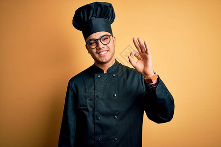 身穿厨具制服和帽子的巴西年轻厨师长在孤立的黄色背景上微笑着正面图片