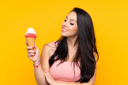 年轻哥伦比亚女孩拿着玉米角冰淇淋在孤立的黄色背景和图片