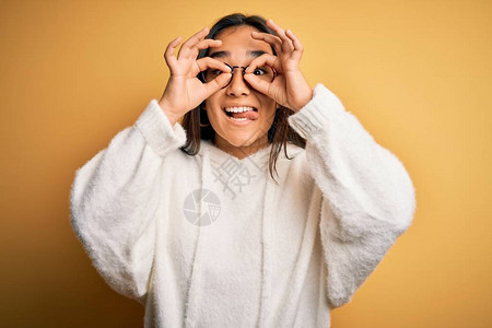 年轻美丽的亚洲女人穿着随身毛衣戴黄色的眼镜像望远镜一样举止正常图片
