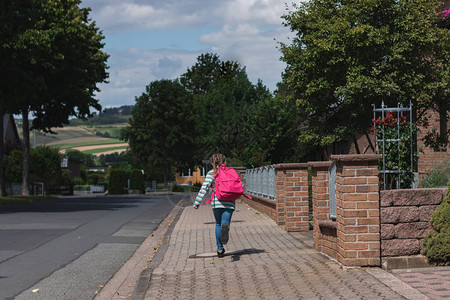 一个背着粉色书包的女孩沿街跑去上学图片