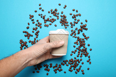 散落的咖啡豆和被手拿住的咖啡杯图片