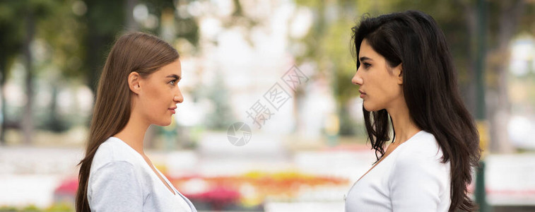 两个女孩朋友在外面站着对峙友谊和女竞争理念图片