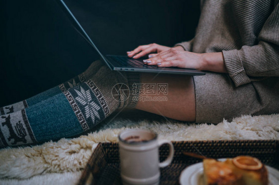 女孩坐在木地板上笔记本电脑和咖啡杯脚穿羊毛袜女人在舒适的家中放松冬季和圣诞假期的概念选择焦图片