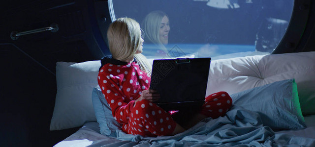 一名年轻女子坐在太空船上的床上时被用视频电话图片