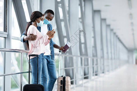 戴着医用口罩的黑人夫妇在机场一起使用智能手机图片