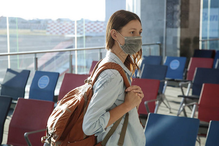 带着防护医用口罩和手提行李在机场等候航班的旅游妇女冠状期间的安全措施图片