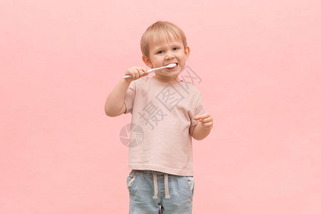 金发小男孩用粉红色背景的牙刷牙关于健康牙龈口腔卫生和牙科治疗以及医生诊所图片
